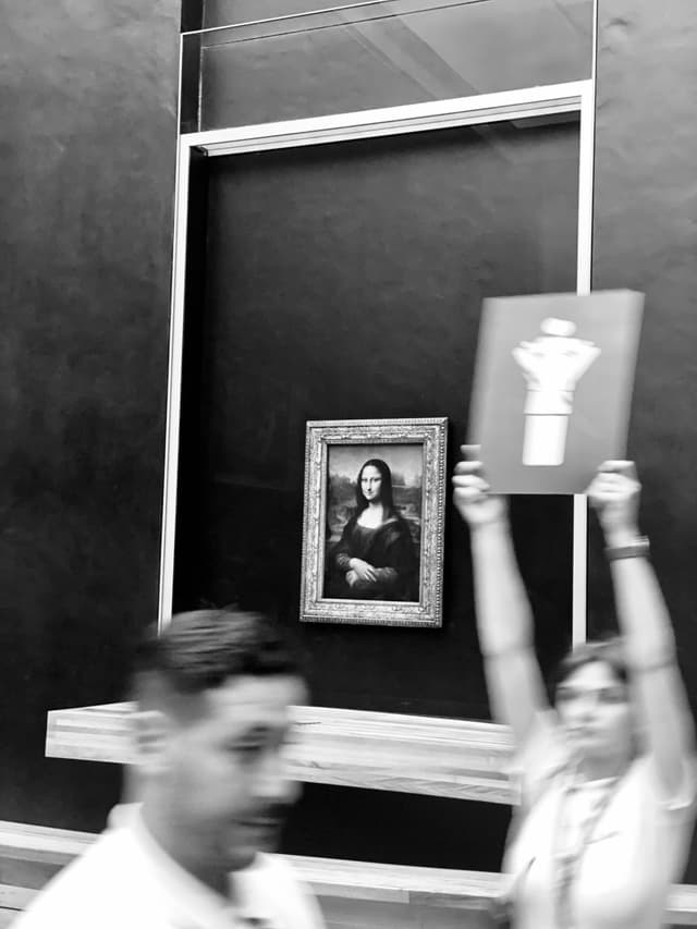 a person holds a protest sign in front of the mona lisa at the louvre museum, captured in a blurred black and white photograph